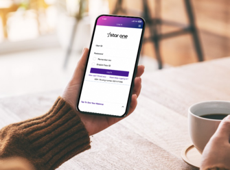 Hands holding mobile phone with Star One login page and coffee