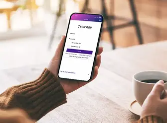 Hands holding mobile phone with Star One login page and coffee