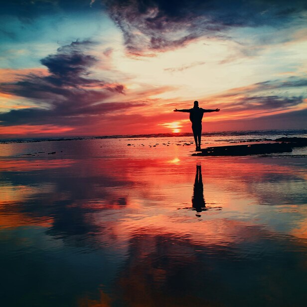 silhouette of a person with arms outstretched in front of a bright sunset