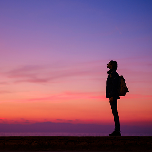 a person standing on a ledge looking up at the sunset