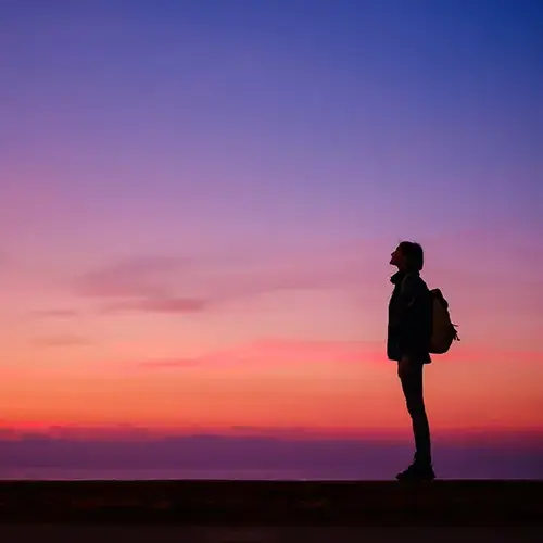 a person standing on a ledge looking up at the sunset