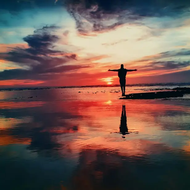 silhouette of person standing on rock surrounded by body of water, photo by Mohamed Nohassi