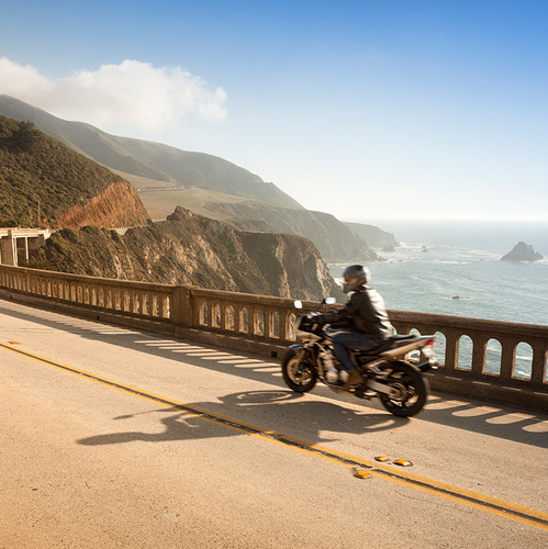 a man riding a motorcycle on a road near a body of water