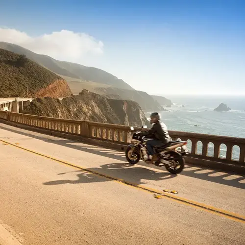 a man riding a motorcycle on a road near a body of water